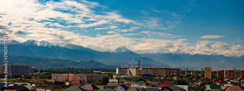 Quadro su tela Scenic panoramic cityscape of Almaty, Kazakhstan with colorful residential buildings and majestic snow-covered Trans-Ili Alatau mountains beneath a blue sky