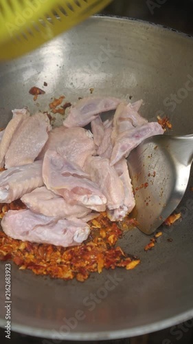 Cooking Thai stir-fried chicken wings (Peek Gai Phad Bai Horapha) by sautéing wings with pounded chili garlic paste, seasoning, and tossing with sweet basil.