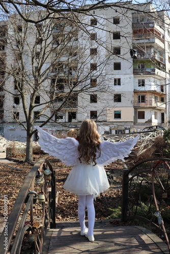Fotografía Little angel with teddy bear against war ruins