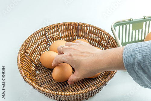 Person hand putting brown chicken eggs into a woven wicker basket isolated on white background