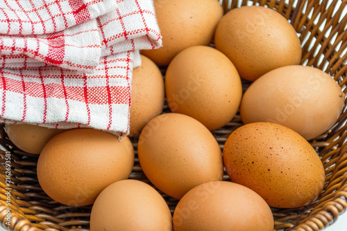 Wicker basket full of brown eggs next to folded kitchen towel isolated on white
