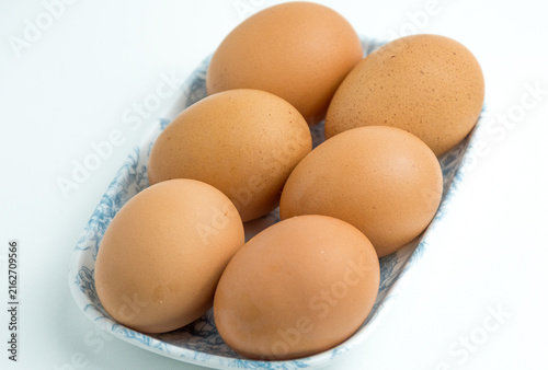Six fresh brown chicken eggs arranged in a small container isolated on white background