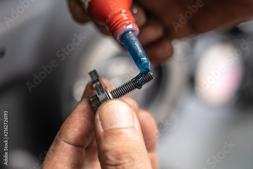 Mechanic applying blue threadlocker fluid to bolt thread before motorcycle engine assembly