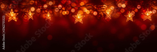 Festive christmas background with glowing golden starshaped fairy lights hanging against a dark red bokeh backdrop, perfect for holiday greeting cards and seasonal celebration designs