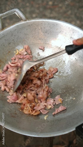 Cooking Thai stir-fried pork (Phad Prik Yuak Sai Moo Chin) by sautéing garlic with sliced pork, seasoning, and tossing with sliced green banana peppers.
