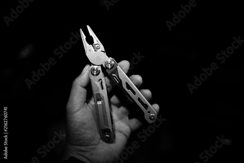 Obraz na plátne Hand holding multifunctional plier tool against dark background, showcasing meta
