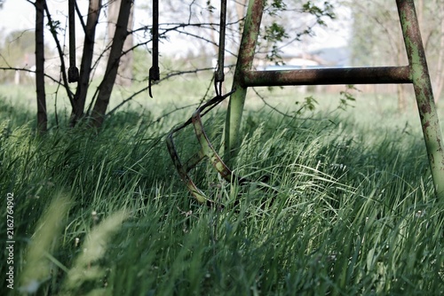 Foto Abandoned broken swing in tall overgrown green grass with rusted frame evoking s