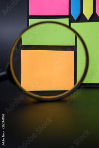 Magnifying glass focusing on a single blank wooden block on black background