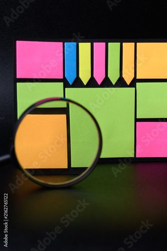 Magnifying glass and sticky tape with neon sticky notes on black background