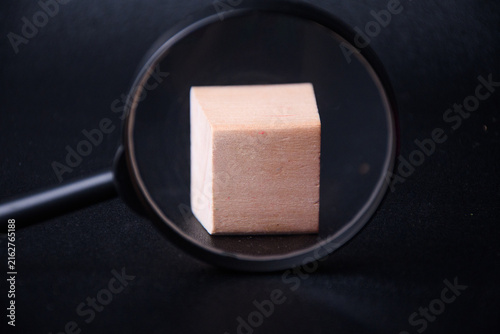 Magnifying glass focusing on a single blank wooden block against black background