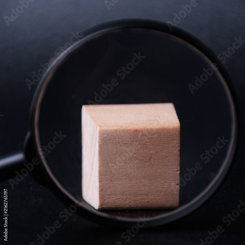 Magnifying glass focusing on a single blank wooden block against black background