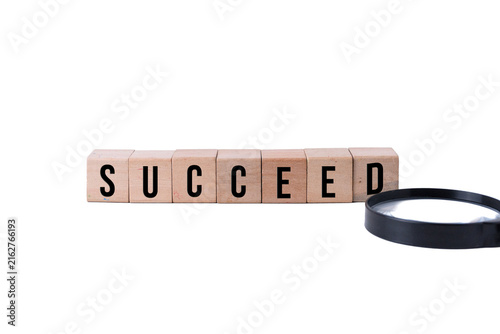 SUCCEED word on wooden blocks and magnifying glass isolated on white background