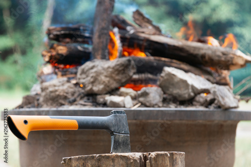Canvastavla camping hatchet embedded in a wooden stump in front of a burning campfire in nat