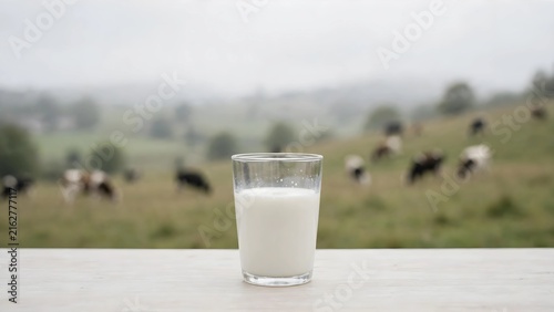 Glass of fresh milk on a table with a blurred rural dairy farm pasture background