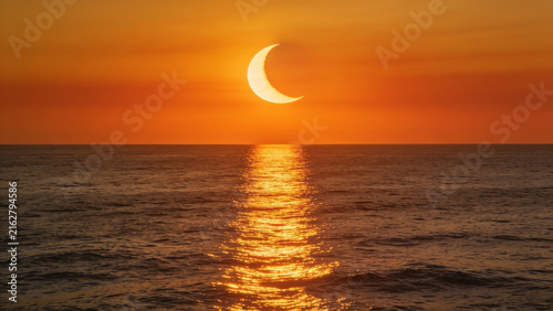 High-resolution professional stock photo of partial solar eclipse at sunset over open ocean with powerful golden reflection on water.