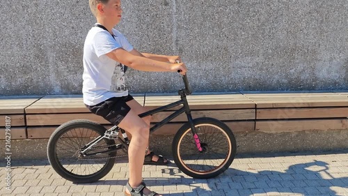 Boy rides a black bicycle on a sunny day in a city park, BMX