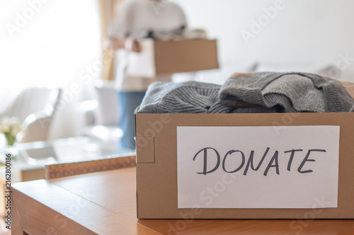 Person filling cardboard box with folded clothes and label donate for charity, decluttering, and giving, promoting help and reuse