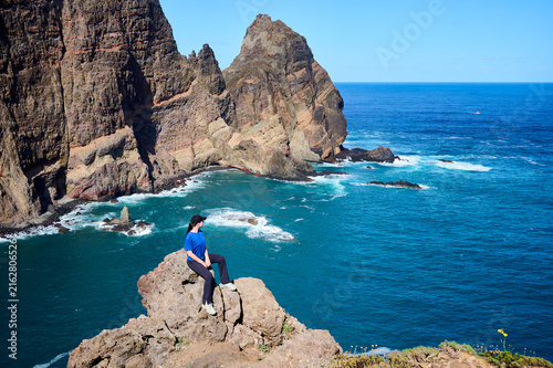 Woman rests on rocky outcrop overlooking vast Atlantic Ocean and dramatic cliffs at Ponta de Sao Lourenco, Madeira. Concept of courage, discovery and personal achievement