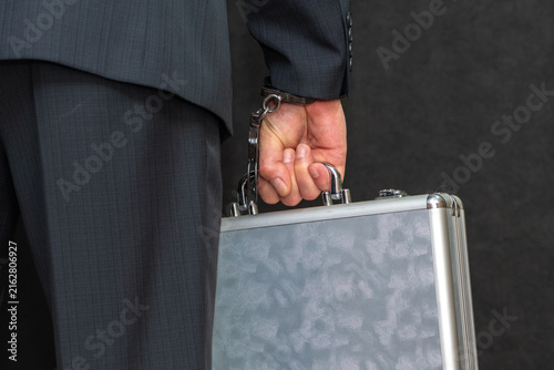 Fotografie Businessman in dark suit holding briefcase while handcuffed behind his back