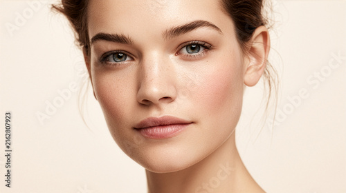A premium beauty advertising portrait of a confident woman looking naturally toward the camera with exceptionally healthy luminous skin