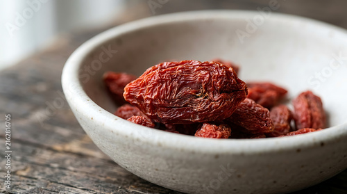 Pile of dried sun-dried tomato pieces inside a ceramic bowl on wooden table