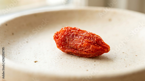 Single dried sun-dried tomato piece placed inside a ceramic bowl macro shot
