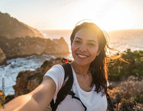 Young woman smiling and taking selfie at scenic coastal location during sunset with ocean view