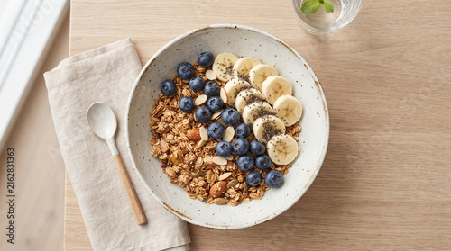 Top Down Flat Lay Photo of Healthy Granola Bowl with Fresh Blueberries Sliced Banana and Chia Seeds on Wooden Table with Cloth Napkin