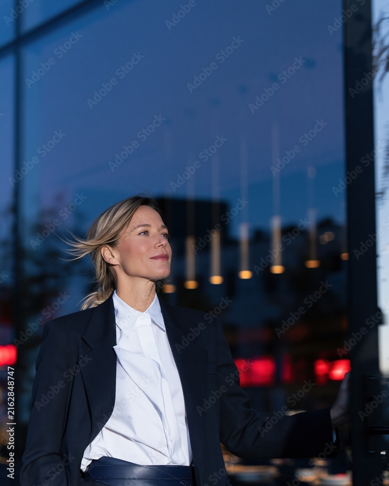 Fototapeta premium Businesswoman pushing open a glass door at a modern restaurant, wearing a tailored charcoal blazer for corporate lifestyle and business services