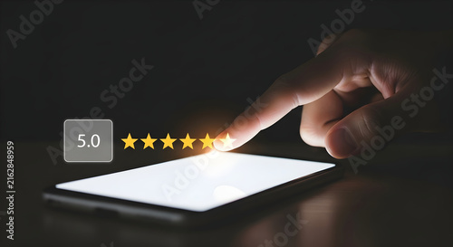 A hand touching a smartphone screen to leave a perfect five star customer review rating and feedback service evaluation in a dark room setting