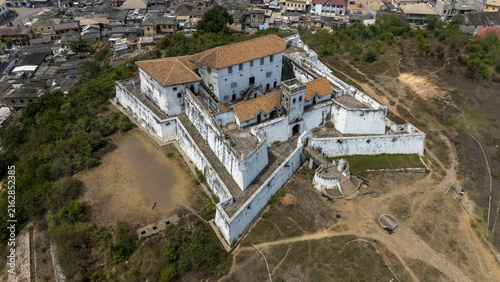 Aerial view of Fort St. Jago, a historic white-walled fortress with orange tiled roofs, situated on a hill overlooking the town of Elmina, Central Region, Ghana.