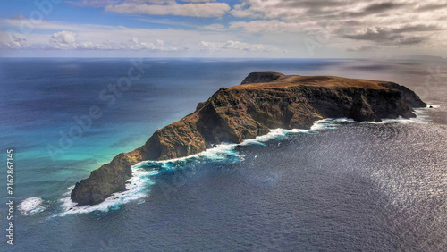 Aerial view of the rugged coastline and rocky cliffs of Porto Santo island surrounded by the deep blue Atlantic Ocean in Porto Santo, Madeira, Portugal.