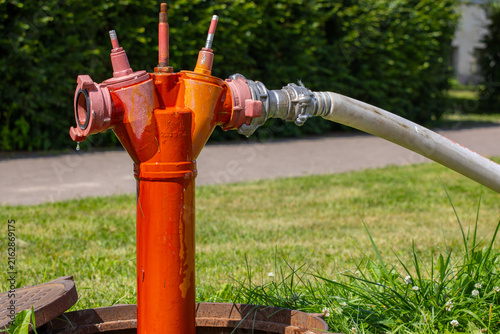 Foto Orange fire hydrant connected to a hose for water supply outdoors
