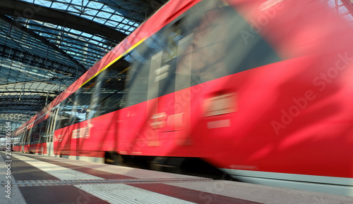 High-speed red commuter train arriving at modern railway station with motion blur