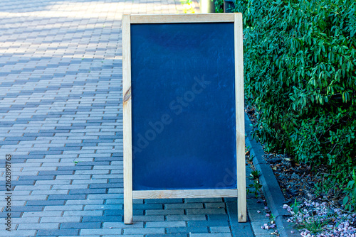 Canvas Print Empty black sandwich board with a natural wood frame placed on a paved sidewalk