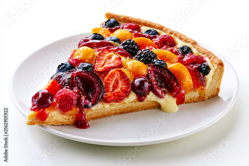 Part de tarte tutti frutti sur fond blanc, sur assiette blanche. Pâte brisée garnie de fruits variés, migaine façon crème pâtissière, surmontée d'un nappage