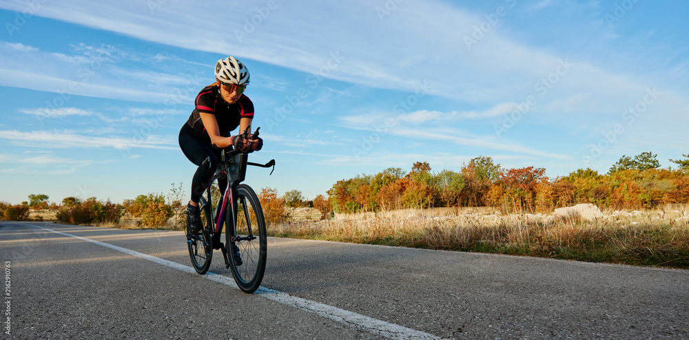 Fototapeta premium Female Cyclist Training on Open Road at Sunrise in Autumn Countryside for Fitness and Endurance