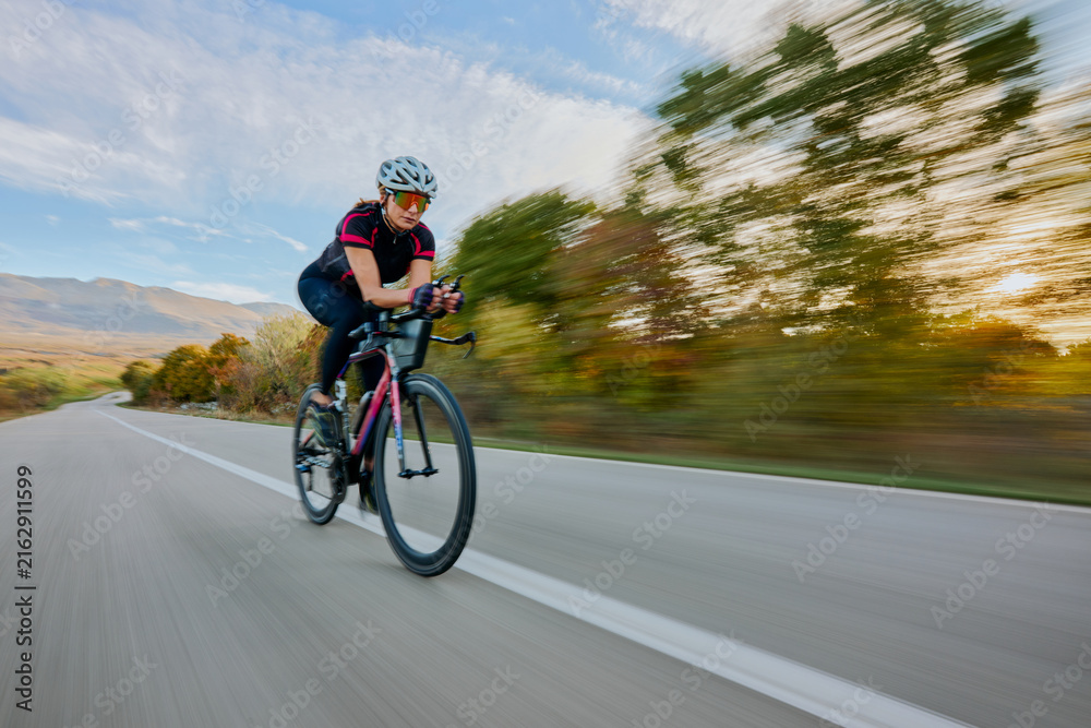 Fototapeta premium Female Road Cyclist Riding Fast On Open Road At Sunset With Motion Blur And Athletic Focus