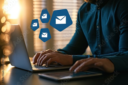 Person typing on laptop with email icons floating above.