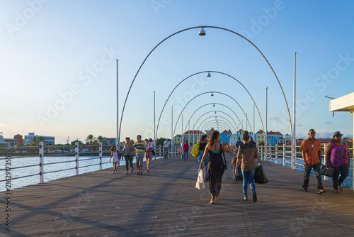 Willemstad, Curacao - 08 November 2014: View of the Queen Emma Bridge with people walking across the wooden pontoon bridge under a clear blue sky.