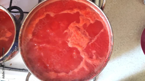 Cooking homemade tomato juice in electric pots at home, close-up view of red tomato puree boiling.