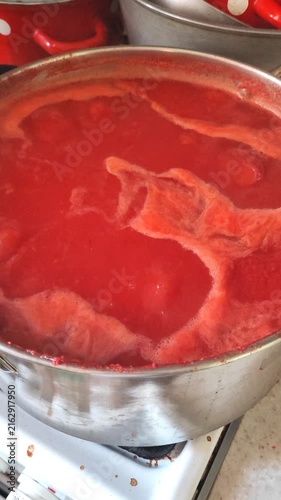 Cooking homemade tomato juice in electric pots at home, close-up view of red tomato puree boiling.