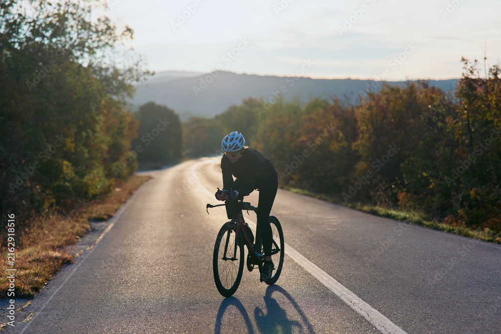 Fototapeta premium Solo Road Cyclist Training At Sunrise On Quiet Rural Road Through Autumn Countryside