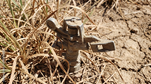 Dry irrigation sprinkler standing in withered grass and cracked ground, symbolizing drought and water scarcity in agriculture