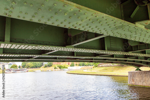 Фотография A close-up view of a large, painted green steel plate bridge seen from a boat passing beneath it