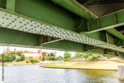 Картината върху платно A close-up view of a large, painted green steel plate bridge seen from a boat passing beneath it
