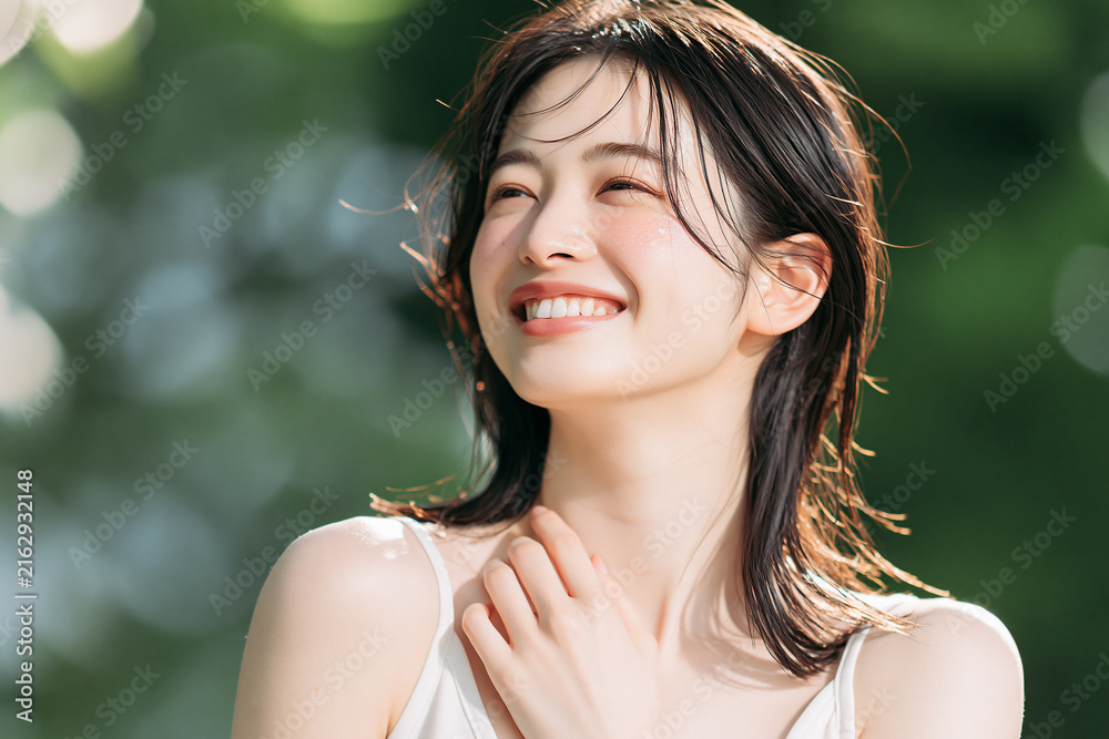 Fototapeta premium きらめく白い肌と爽やかな笑顔の日本人女性。みずみずしい緑の自然の背景。美容、スキンケア、オーラルケア、デンタルケア素材