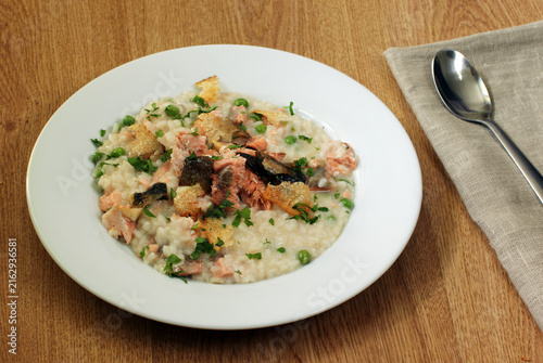 Salmon risotto with green peas and crispy salmon skin topping served on white plate
