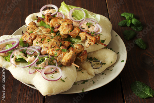 Grilled chicken skewers with fresh pita bread, red onions, lettuce and yogurt sauce on a dark wooden table
