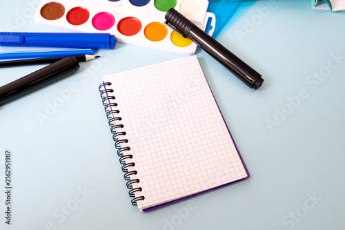 Notebook, pens, pencil, ruler, watercolor paints and paper arranged on a tabletop with open space for text